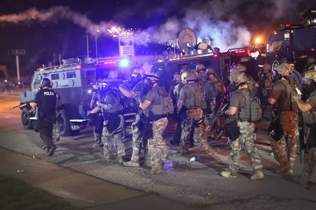 Police in Ferguson, Missouri advance on protesters wearing military gear. The feds could still give police departments armored vehicles like the ones pictured under President Obama's just-announced policy change.